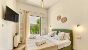 Une chambre avec un lit recouvert d’un tissu vert, un téléviseur à écran plat fixé au mur, une porte-fenêtre coulissante donnant sur un balcon et une petite table de chevet agrémentée d’une plante.