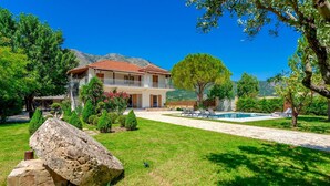 Une maison à deux étages avec un balcon, une piscine et un paysage montagneux en arrière-plan.