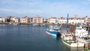 Ein Hafen mit vertäuten Booten, Gebäuden im Hintergrund und einem klaren Himmel.