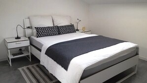 Ein modernes Schlafzimmer mit einem Bett, weißen Nachttischen, einer Lampe und einem Streifen Teppich.