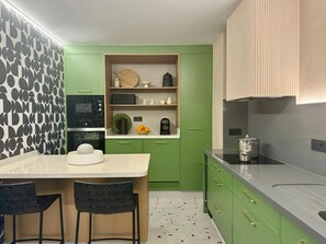 Una cocina moderna con gabinetes verdes, una encimera blanca y dos taburetes negros.