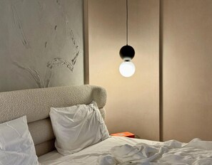 Een slaapkamer met een gestructureerd hoofdeinde, een hanglamp en een net opgemaakt bed.