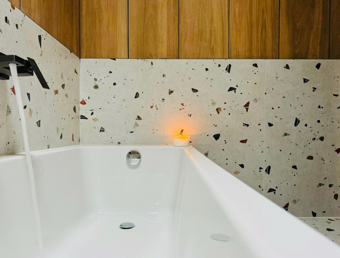 A white bathtub with a speckled tile wall and wooden paneling above.