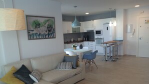 Ein modernes Wohnzimmer mit einer Couch, einem Essbereich mit Tisch und Stühlen sowie einer Küche mit weißen Schränken und Geräten.