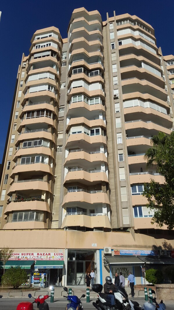 A multi-story residential building with balconies, a ground-level commercial establishment, and a clear sky.