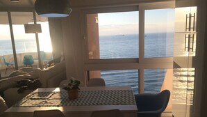 Eine moderne Küche mit großem Fenster zum Meer, einem Essbereich mit Tisch und Stühlen sowie ein Blick auf ein Schiff in der Ferne.
