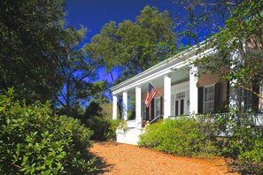 A white building with columns and a porch, surrounded by greenery and trees. - Sunnyside Bed & Breakfast (Natchez)
