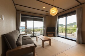 Una sala de estar moderna con un sofá, una mesa de centro de madera y un televisor. Amplias ventanas ofrecen vistas al exterior.