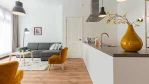 Un salon moderne avec un canapé gris, un fauteuil jaune et une table basse en bois. On y trouve également un coin cuisine avec un évier et un vase de fleurs posé sur le comptoir.
