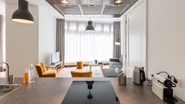 Une chambre d’hôtel moderne dotée d’un coin cuisine, d’une table à manger, d’un canapé et d’une grande fenêtre avec des rideaux.