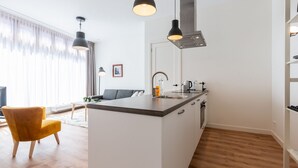 Une cuisine moderne avec un îlot central, un coin repas avec une chaise jaune et un espace de vie comprenant un canapé et un tableau.