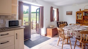 A kitchen with a microwave, a dining area with a table set for four, and a wooden cabinet with a bowl on top. - Disabled and family friendly bungalow on working farm in East Sussex countryside (Mayfield)