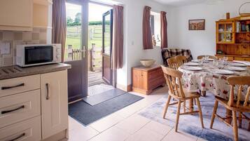 Une cuisine équipée d’un four à micro-ondes, un coin repas avec une table dressée pour quatre personnes, et un meuble en bois sur lequel est posé un saladier.