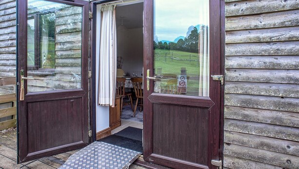 A wooden cabin with a large open door, a small porch area, and a view of a grassy field. - Disabled and family friendly bungalow on working farm in East Sussex countryside (Mayfield)