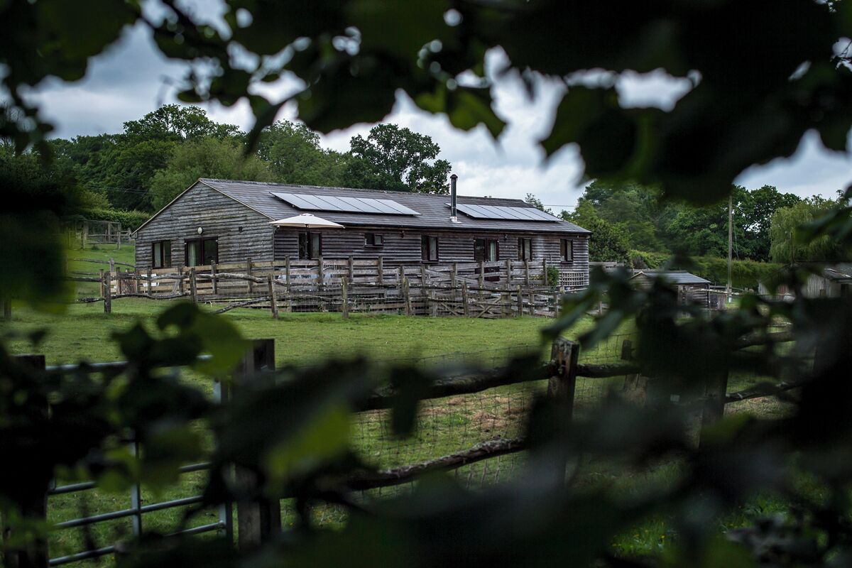 A rustic wooden barn with solar panels on the roof, surrounded by a fenced pasture.