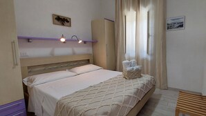 A bedroom with a bed, a headboard, a bedside table with towels, a wardrobe, and a window with curtains. - Brand new apartment with veranda (Peschici)