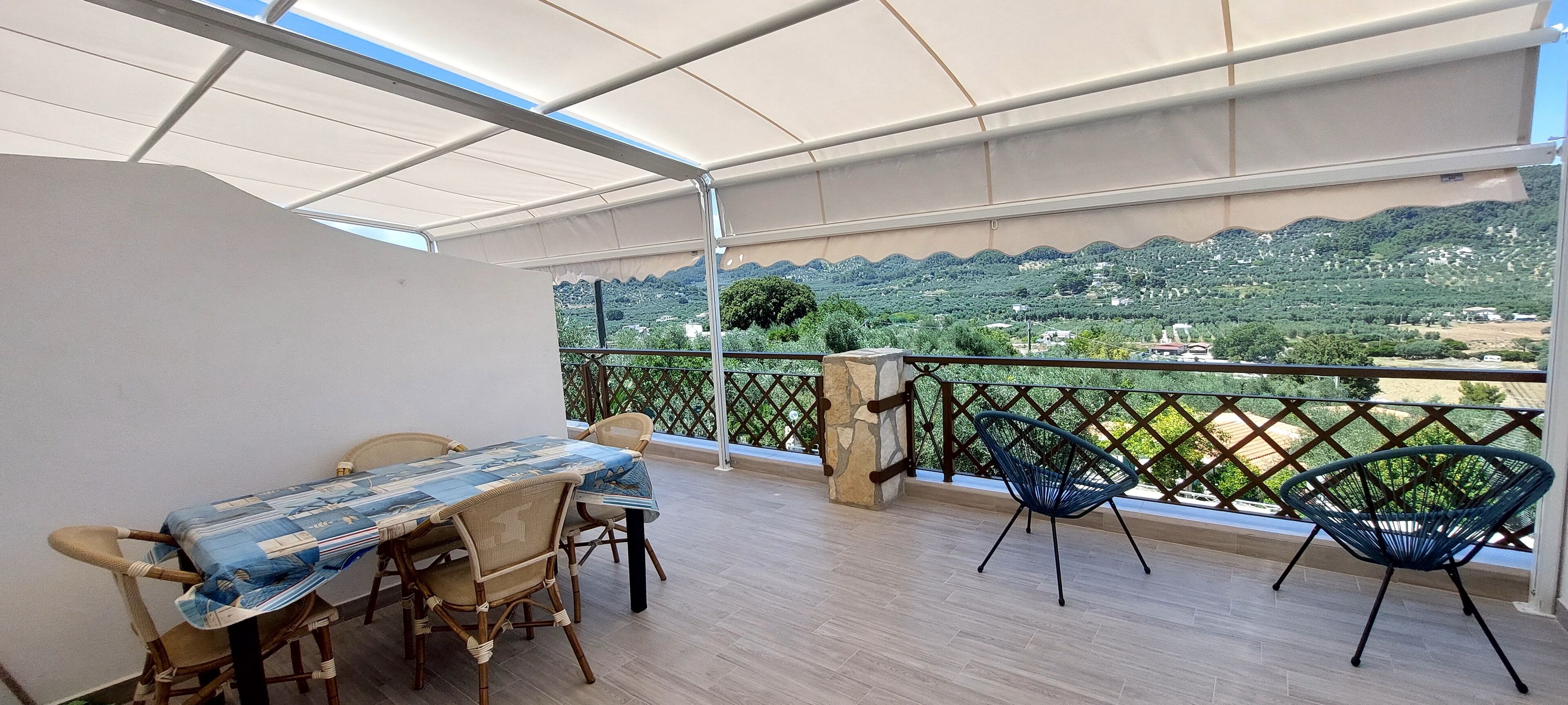 A balcony with a table and chairs, a view of a green landscape, and a white canopy.