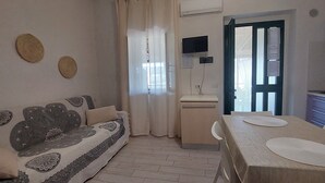 A living room with a sofa, a dining table with placemats, a kitchen area with a stove, and a door leading outside. - Brand new apartment with veranda (Peschici)