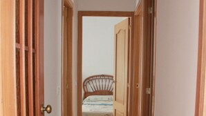 Un couloir étroit, avec des portes en bois, mène à une chambre à coucher où se trouve un lit.