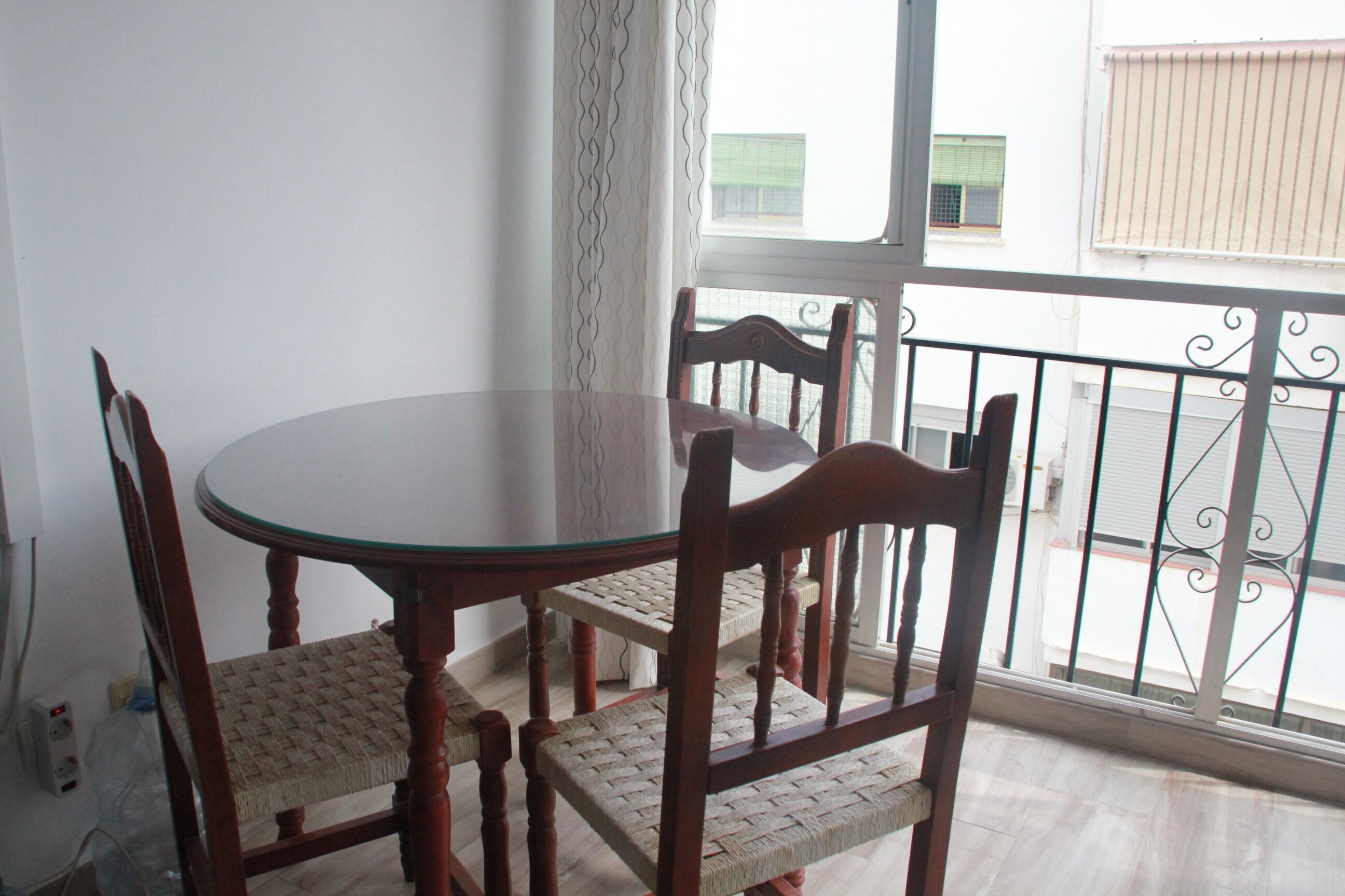 Een eetgedeelte met een ronde tafel en vier houten stoelen met geweven zittingen.