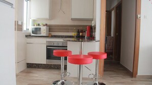 Une cuisine moderne avec des meubles blancs, un four à micro-ondes et une cuisinière à gaz. On y trouve trois tabourets de bar rouges et un comptoir sur lequel sont disposés divers objets.
