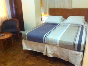 Une chambre d’hôtel avec un lit en bois, une petite table ronde et une chaise.