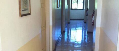 Un pasillo largo y estrecho con baldosas de diseño en el suelo, un cuadro en la pared izquierda y un extintor en la derecha.
