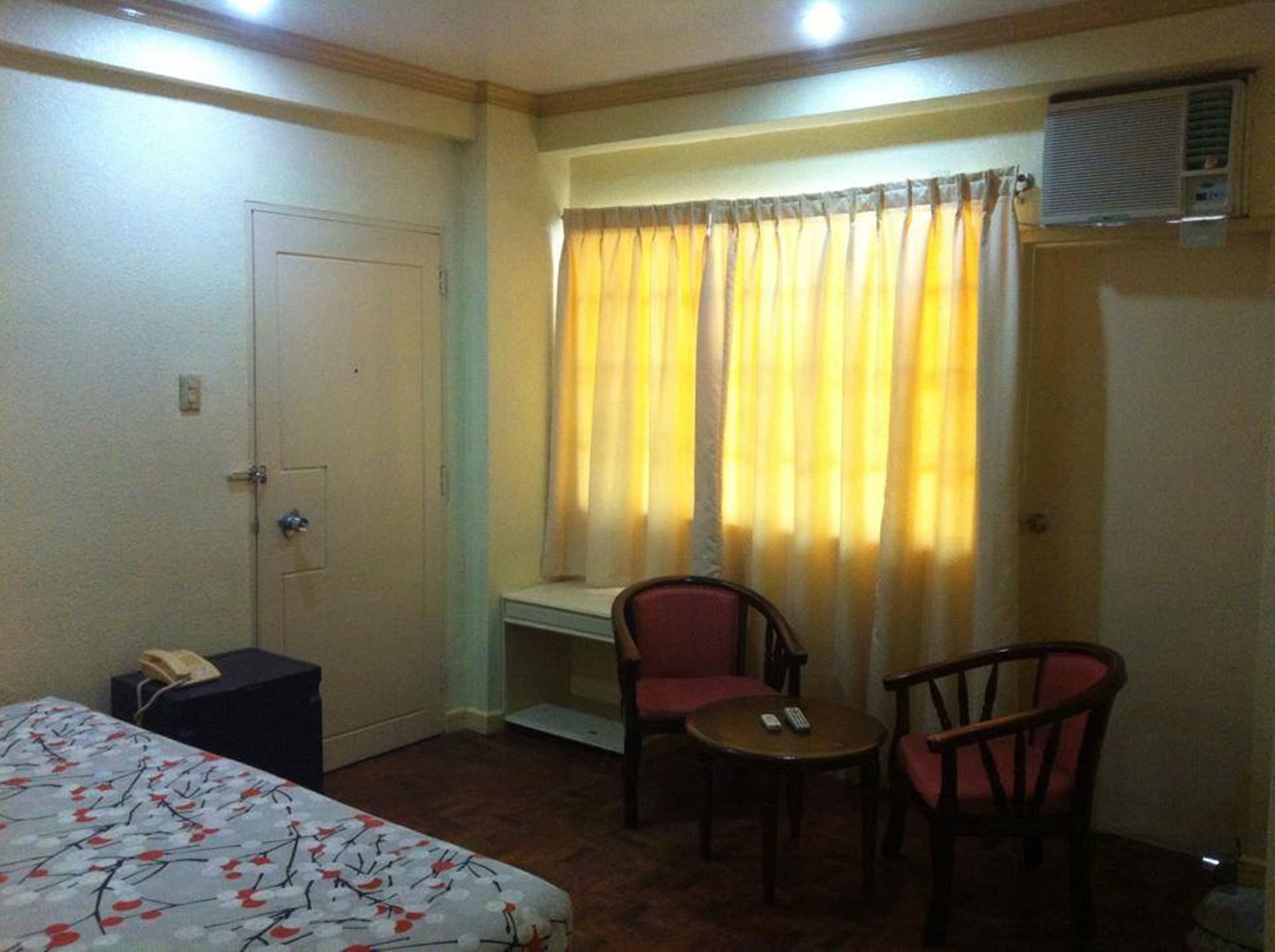 Habitación de hotel con cama, escritorio con teléfono, pequeña mesa con sillas y ventana con cortinas.