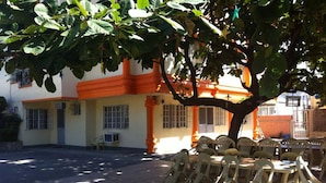 A building with a yellow facade and orange accents, outdoor seating with plastic chairs, and a tree providing shade. - Tondaligan Beach Hotel (Dagupan)