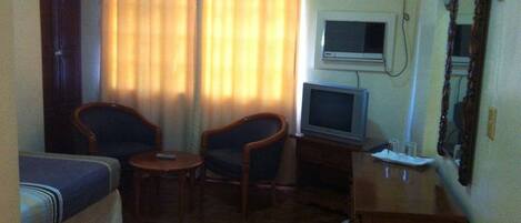 Una habitación de hotel pequeña con dos camas individuales, un televisor, un escritorio y dos sillas.