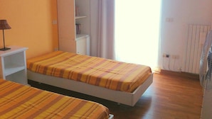 Ein Zimmer mit zwei Betten, einem Kleiderschrank und einem Fenster mit Vorhängen.