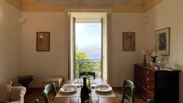 Ein Esszimmer mit einem langen Tisch, gedeckt für vier Personen, einer Chandelüster und Blick durch ein Fenster.
