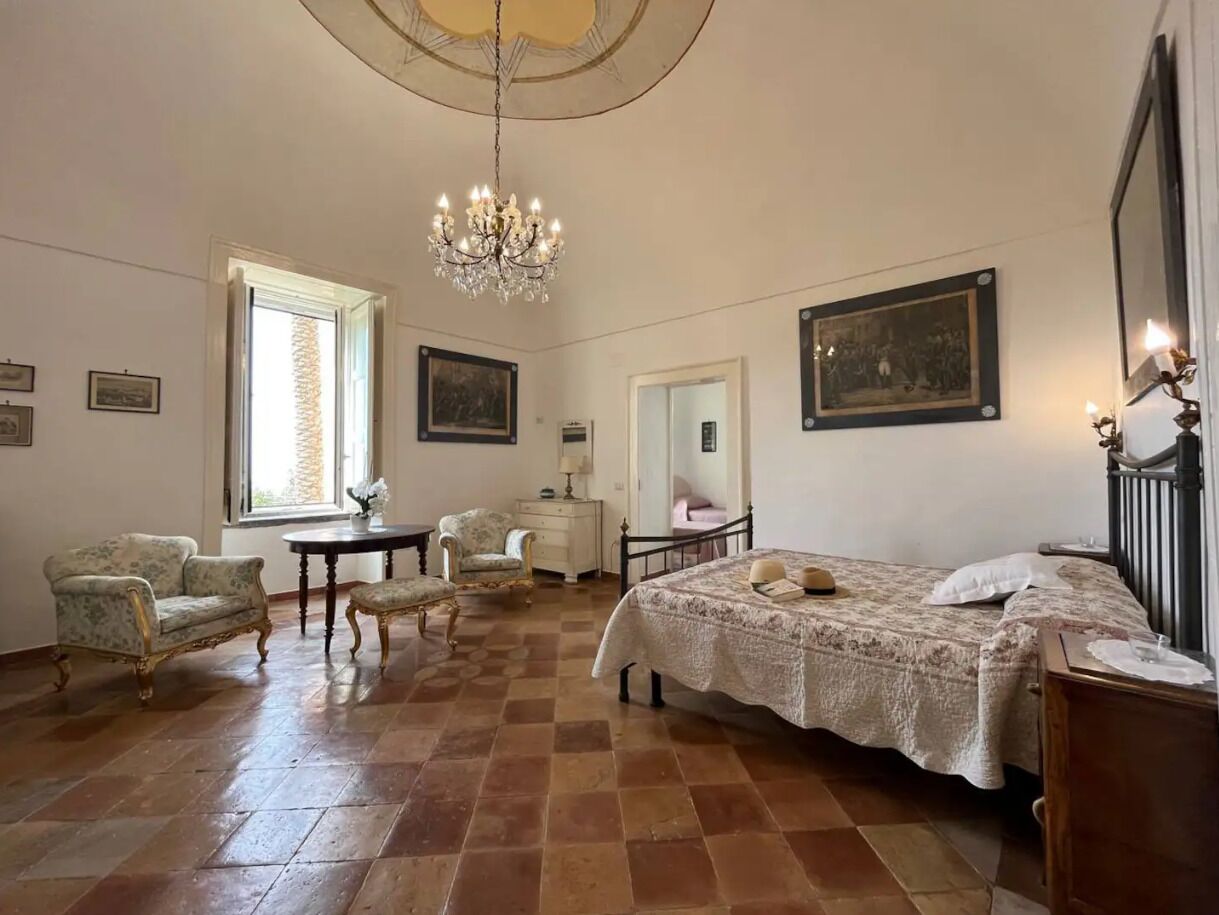 Ein Schlafzimmer mit einem großen Bett, einer Kandelaber, einem Schreibtisch und einem Sessel.