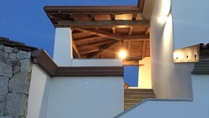 A modern building with a stone wall on the left and a white facade with a wooden roof structure. - Residenza Limpiddu with Swimming Pool and Panoramic View - Recent, All Amenities (08020 Budoni)