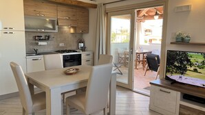 A modern kitchen with a dining area, a TV, and a sliding glass door leading to an outdoor patio. - Residenza Limpiddu with Swimming Pool and Panoramic View - Recent, All Amenities (08020 Budoni)