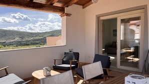 A balcony with wooden furniture, a glass door leading to an interior space, and a view of green hills. - Residenza Limpiddu with Swimming Pool and Panoramic View - Recent, All Amenities (08020 Budoni)