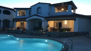 A large swimming pool with a stone border, a patio area with outdoor furniture, and a multi-story building with arched windows and a tiled roof. - Residenza Limpiddu with Swimming Pool and Panoramic View - Recent, All Amenities (08020 Budoni)