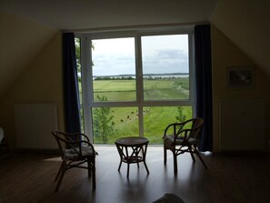 Ein Zimmer mit einem großen Fenster, zwei Korbstühlen und einem kleinen runden Tisch.