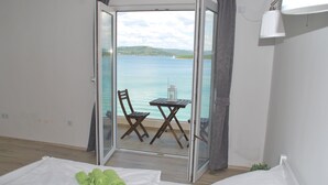 Een kamer met een bed, een tafel en een stoel, nabij een schuifdeur die uitkomt op een balkon met uitzicht op zee.