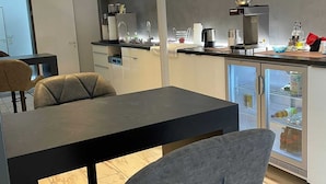 A modern kitchen with a dining area, featuring a black table and grey chairs, a built-in stove, and a refrigerator with a glass door. - SMC Münster - double room (Münster)