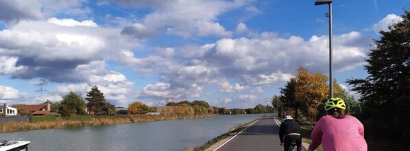 Un río con ciclistas en un camino pavimentado, árboles y cielo despejado.