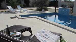 A poolside area with lounge chairs, a table with a bottle and glasses, and a tiled pool. - Villa Mediteran Liznjan home with private pool in Istria
 (Ližnjan)