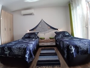 Un dormitorio con dos camas, una decoración de mosquitero colgante, un armario de madera y una mesita con cajones.