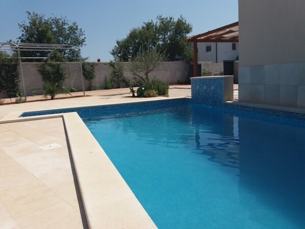 Piscina rectangular con agua azul cristalina, rodeada por un deckado de baldosas.