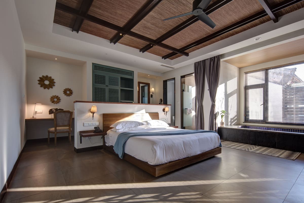 A modern bedroom with a wooden ceiling, a large bed, a desk, and a window with curtains.