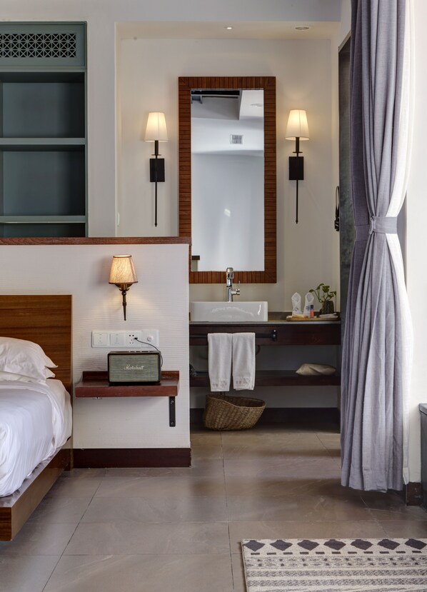 A modern hotel room with a bed, bedside table, lamp, radio, mirror, sink, towel rack, and a patterned rug. - Vangen Spa Hotel (Miyun)