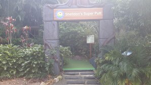 A stone archway with a sign reading "Sheldon's Super Putt" and a small green area beneath it. - Gold Coast Family Apartment (Mermaid Beach)