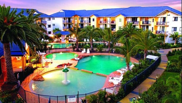A hotel with a large outdoor swimming pool, multiple balconies, and lush greenery. - Gold Coast Family Apartment (Mermaid Beach)
