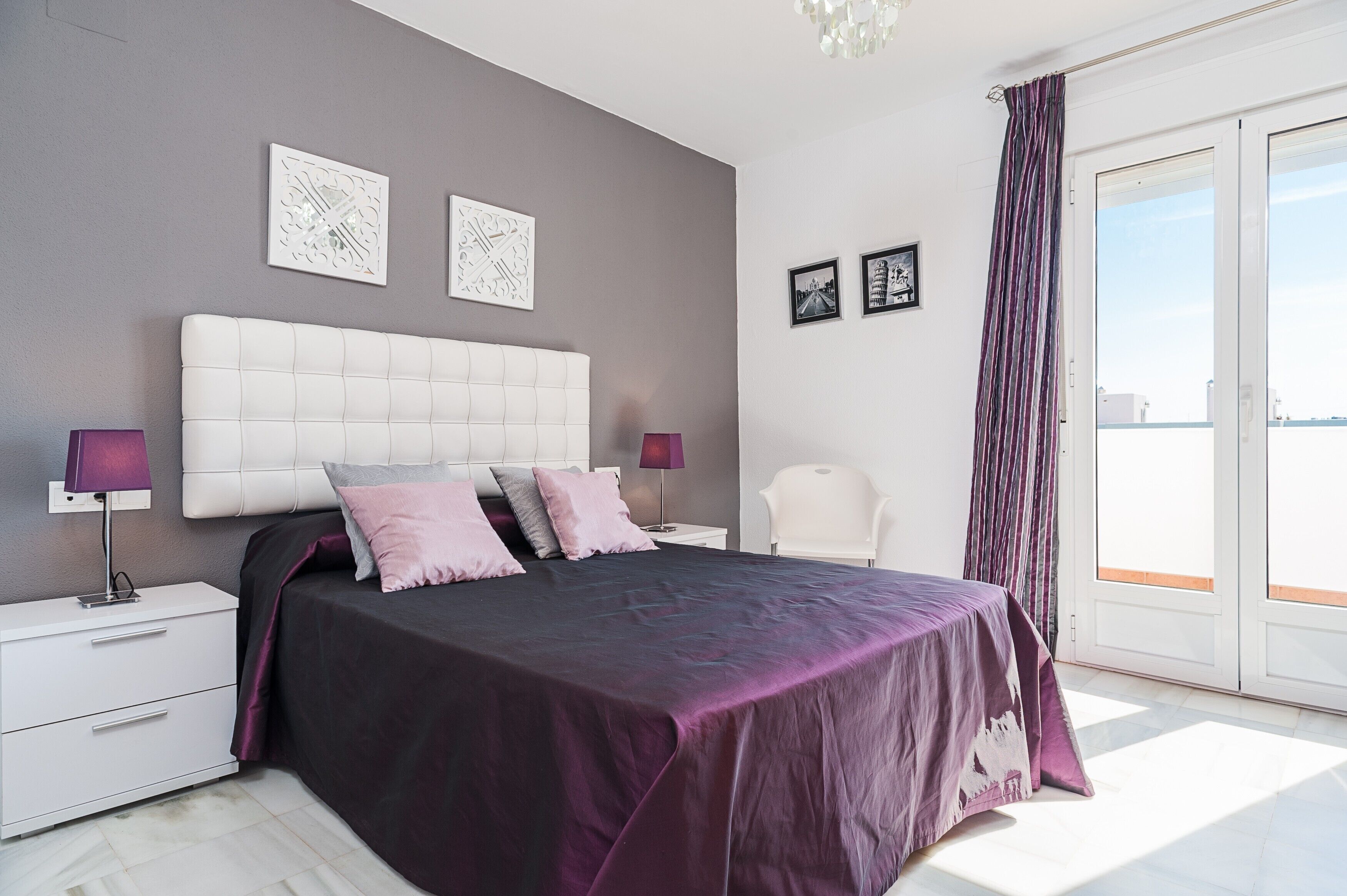 Une chambre à coucher avec un grand lit, deux tables de chevet, une commode, une chaise et une vue sur l’extérieur, accessible par une porte coulissante.