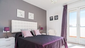 A bedroom with a large bed, two bedside tables, a nightstand, a chair, and a view through a sliding door.